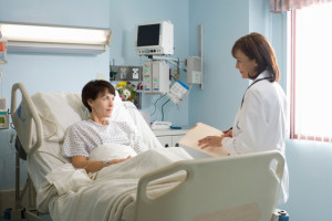 Female doctor talking to female patient lying in hospital bed